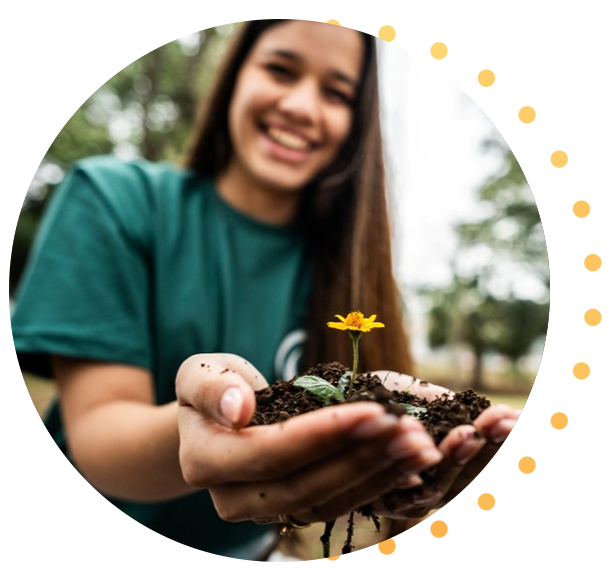 Personne tenant un petit tas de terre avec une fleur jaune en pleine floraison et un jeune plant à l'extérieur, fond flou