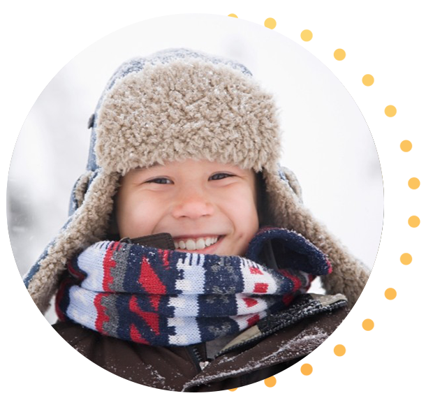 Personne portant un chapeau doublé de fourrure et une écharpe à motifs dehors sous la neige avec des arbres flous en arrière-plan