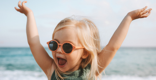 Une jeune fille les mains en l’air et à la plage pose pour une photo.