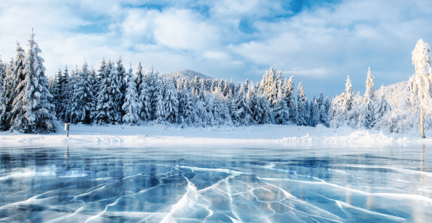 Fissures à la surface de la glace bleue. Lac gelé dans les montagnes d'hiver. Il neige. Les collines de pins. Carpates Ukraine Europe.
