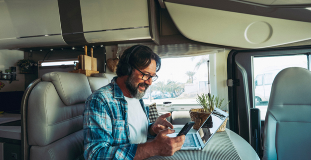 Un homme semble passer un appel vidéo. Il sourit en tenant son téléphone, ses mains sont animées et la conversation semble passionnante. Un portable ouvert sur la table du VR. L’intérieur du VR est confortable et moderne.