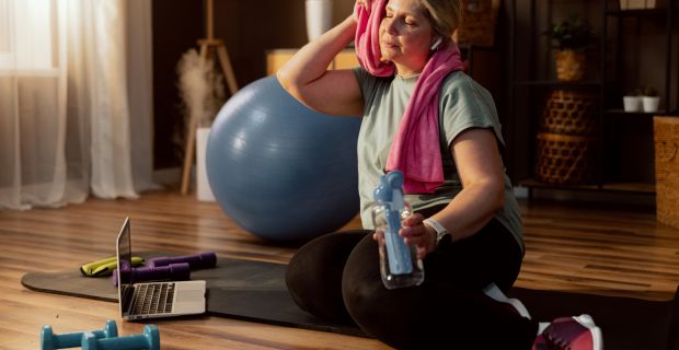 Une femme dans la quarantaine essuie son front après avoir terminé ses exercices à la maison.