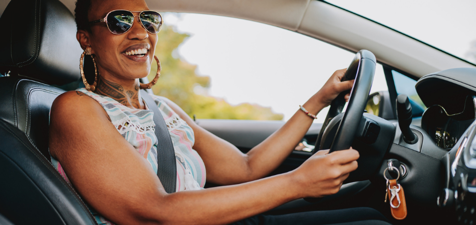 Une personne heureuse économisant sur l’entretien de sa voiture à l’intérieur de son véhicule, au volant et vêtue d’un t-shirt sans manches.