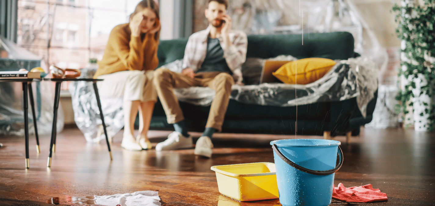 Dégâts d’eau dans un salon, avec des seaux sur le sol et des meubles recouverts de plastique pour retenir les fuites.