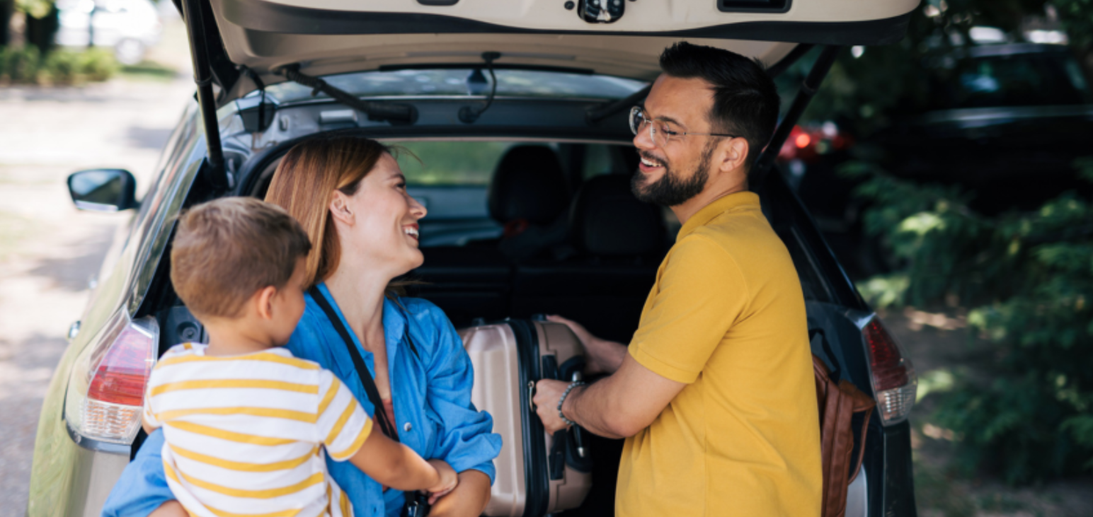 Une famille heureuse de trois personnes sourit et discute tout en chargeant le coffre de leur voiture pour un voyage en famille. 