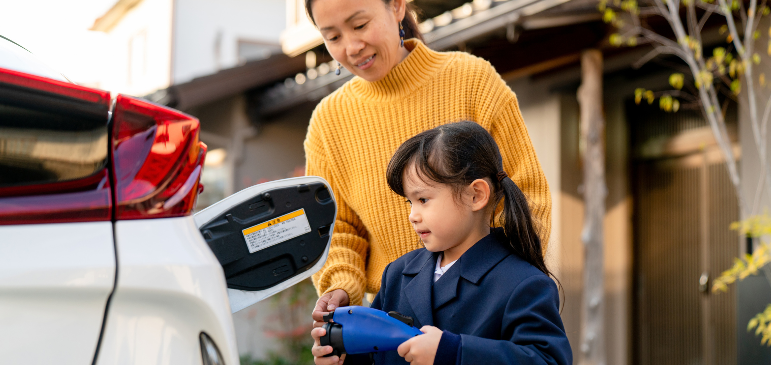 Un parent et un enfant rechargent un véhicule électrique dans l’entrée de leur maison.