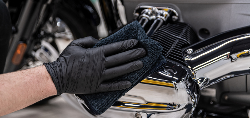 Une main gantée nettoie le moteur d’une moto lors des préparatifs pour le remisage hivernal.  