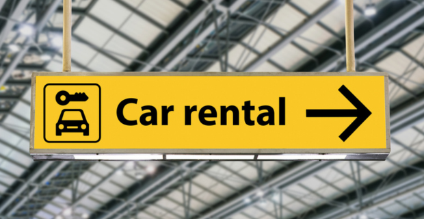 Une enseigne jaune dans un aéroport affichant l’image d’une voiture et d’une clé avec les mots « location de voitures » ainsi qu’une flèche.