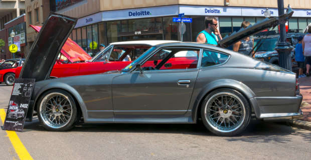 Une Nissan Datsun 240Z gris foncé avec le capot relevé lors d’un salon automobile. 