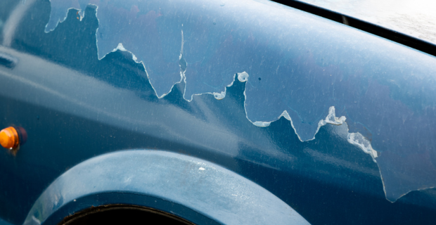 De la peinture s’écaille au-dessus du puits de roue d’une voiture bleue en raison des dommages causés par le soleil.