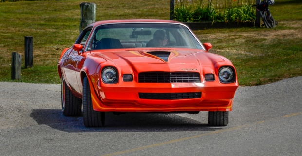 Une Chevy Camaro 1980 orange tournant sur une route de campagne.