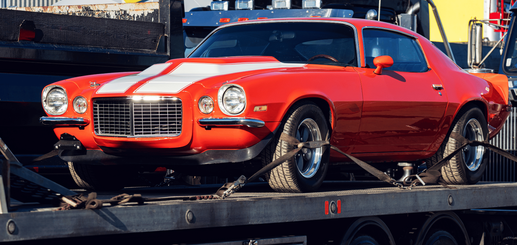 Une voiture musclée rouge des années 1970 sur une remorque à plateau pendant son transport.
