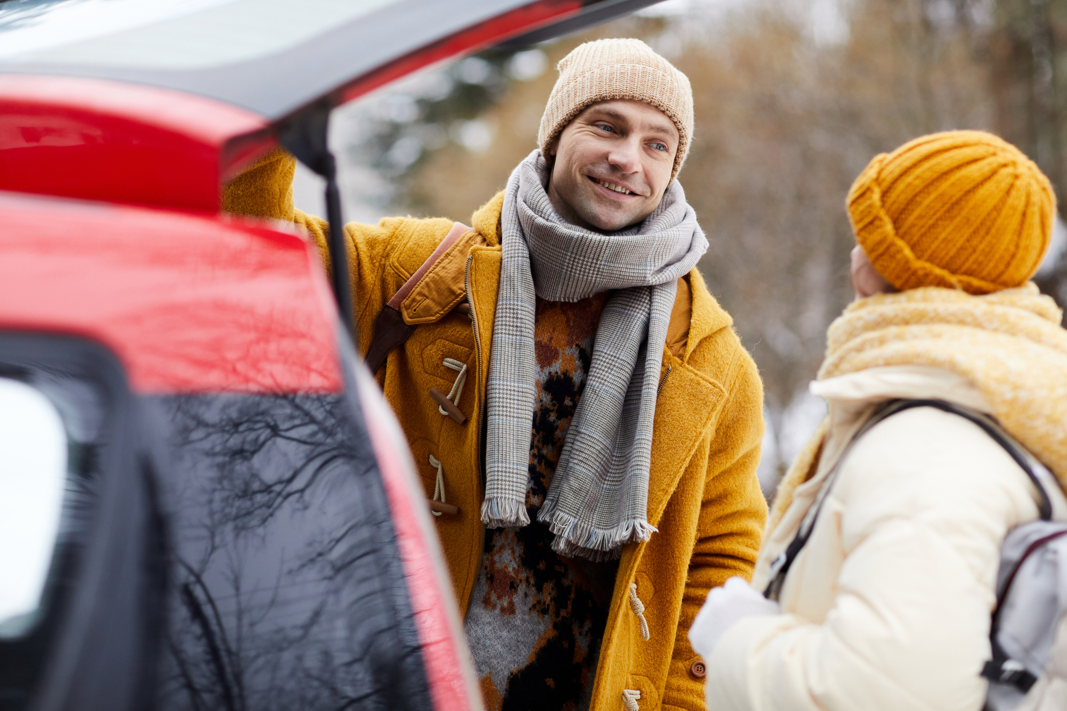 Un couple souriant debout devant le coffre ouvert de sa voiture en hiver