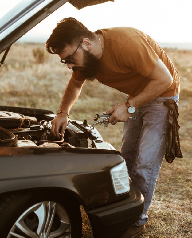 Un homme barbu d'une vingtaine d'années travaillant sur sa voiture.