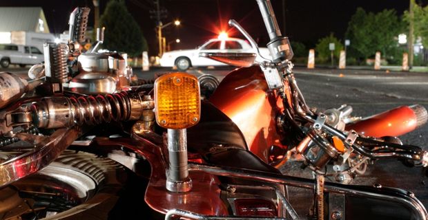 A motorcycle lies on its side on the road. In the background a police car is parked with its lights flashing.