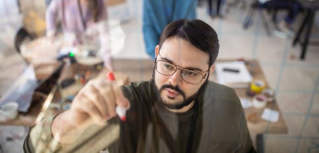 Un homme corpulent avec des lunettes, une barbe et une moustache écrit sur un tableau effaçable à sec.