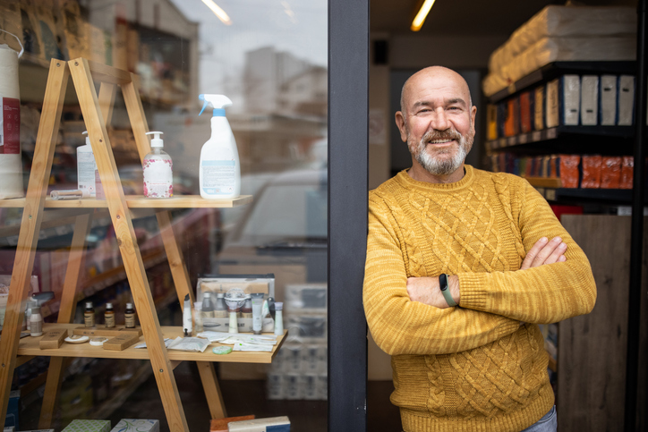 Un homme souriant se tient debout, les bras croisés, devant un magasin.