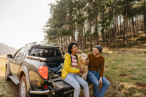 Un couple est assis sur le portail de leur camionnette et caresse leur chien.