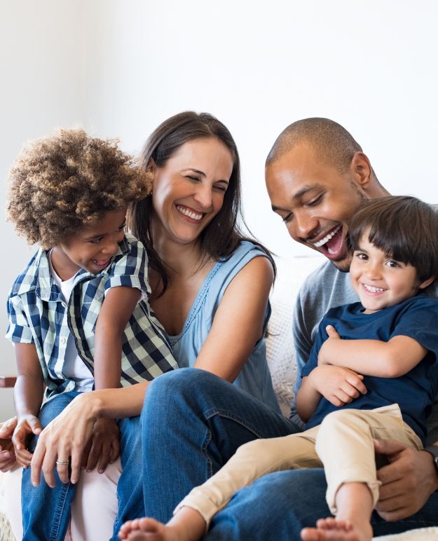 Des parents et deux jeunes enfants rient ensemble dans leur salon.