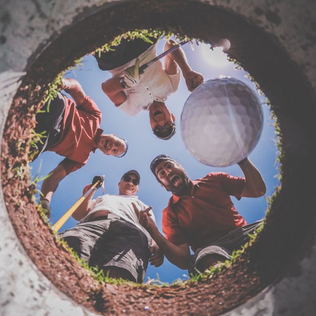Un groupe d’amis regardant dans le trou et applaudissant lorsque leur balle de golf entre.