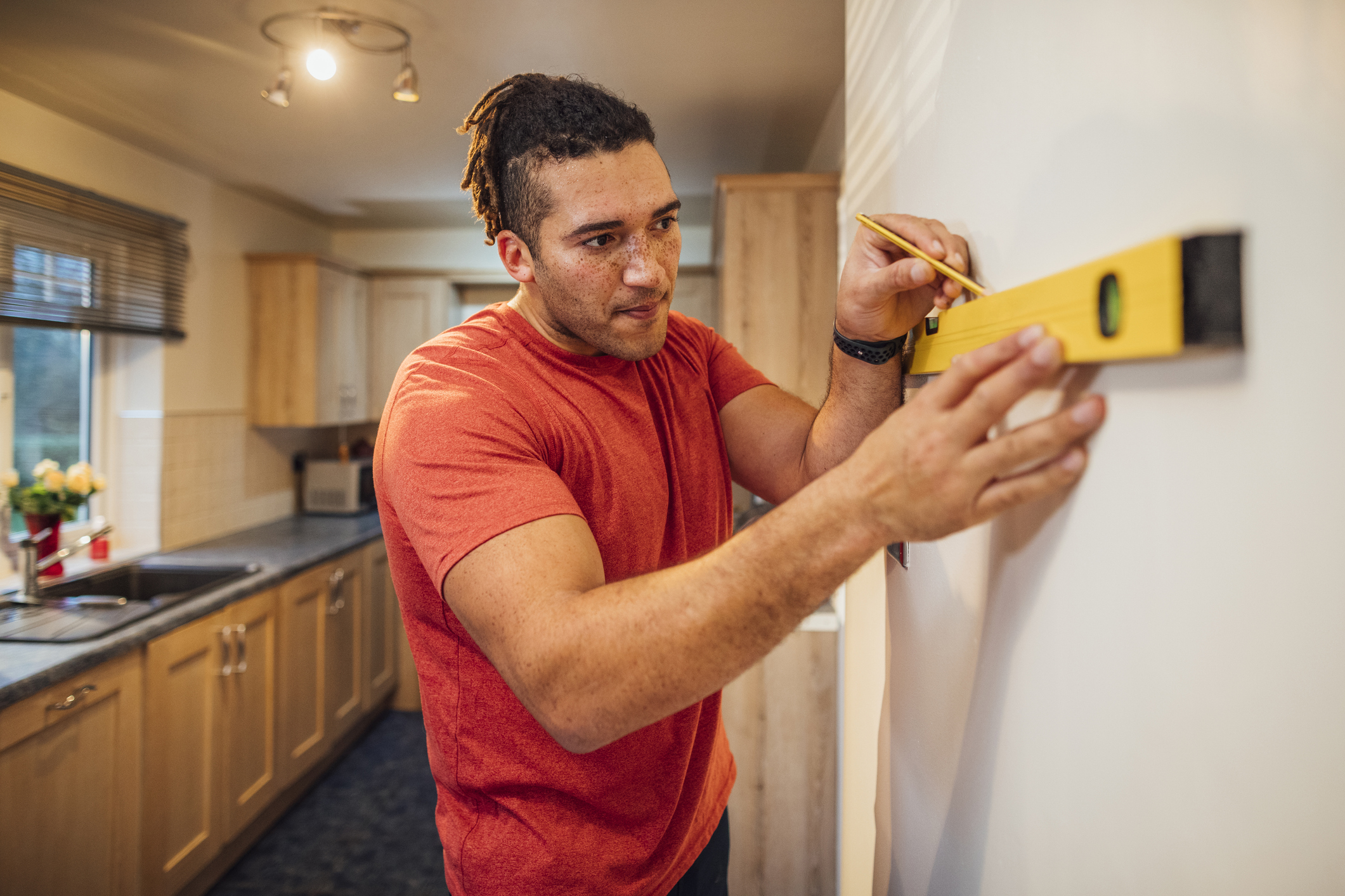 Man drawing line above level tool on kitchen wall in home