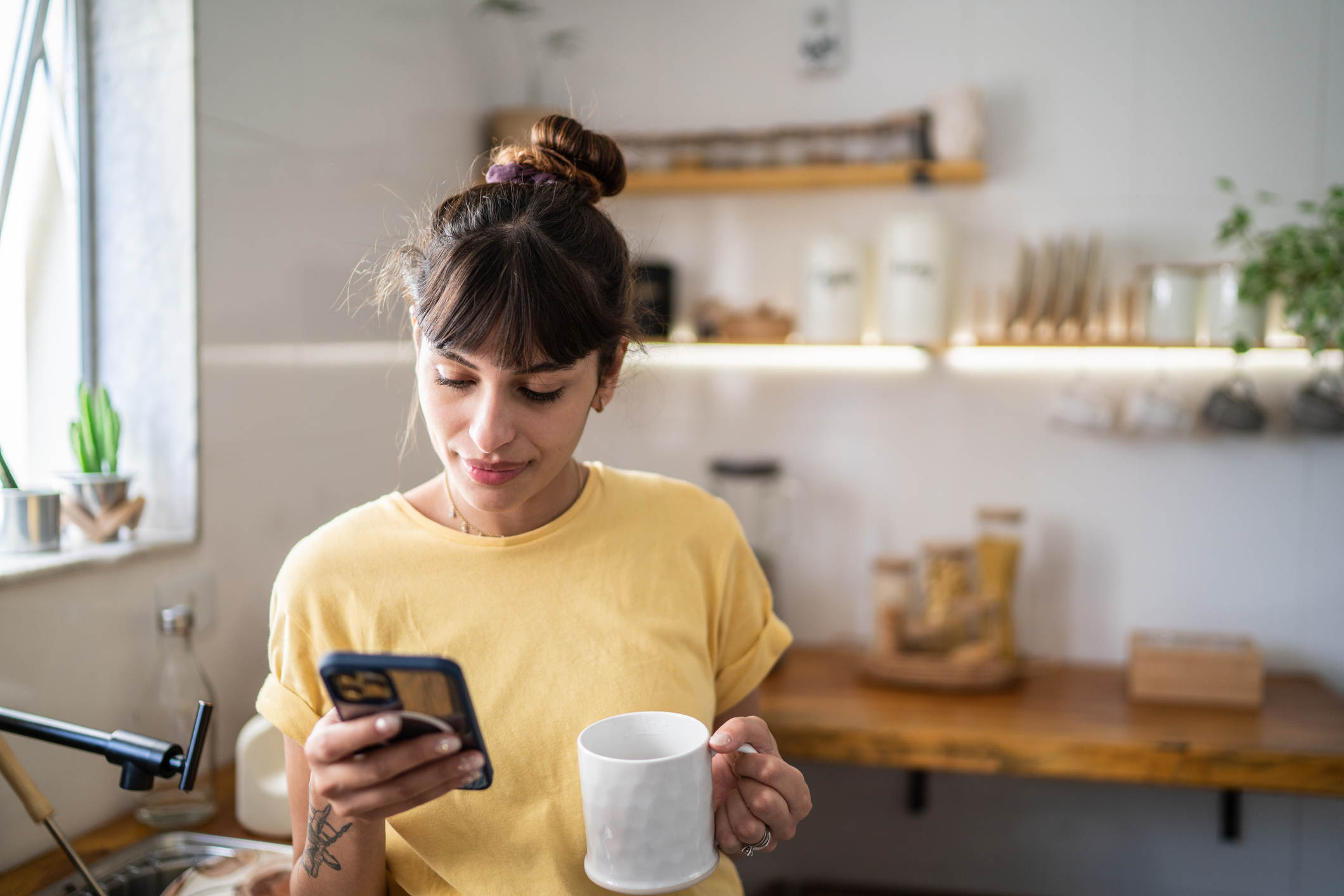 Jeune femme utilisant son téléphone tout en buvant dans une tasse chez elle