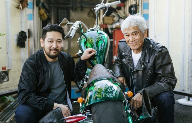 Un homme en blouson aviateur et son grand-père sourient, posant de part et d'autre d'un croiseur.