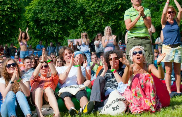 Lors d’un événement en plein air, un groupe est assis sur l’herbe et applaudit.