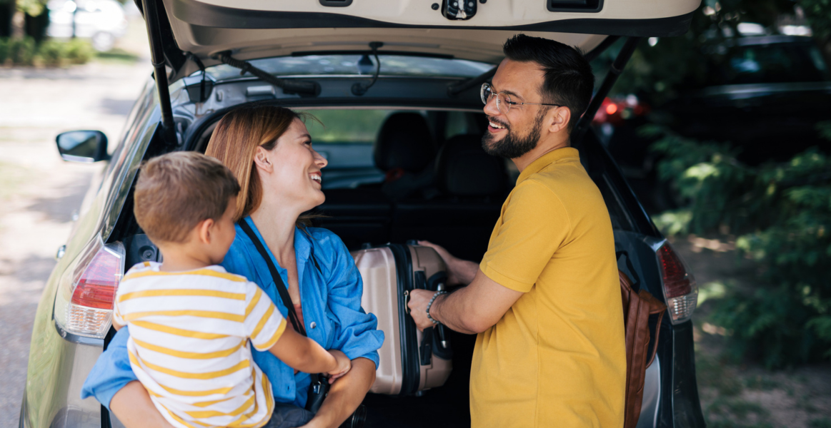 Une famille heureuse de trois personnes sourit et discute tout en chargeant le coffre de leur voiture pour un voyage en famille. 