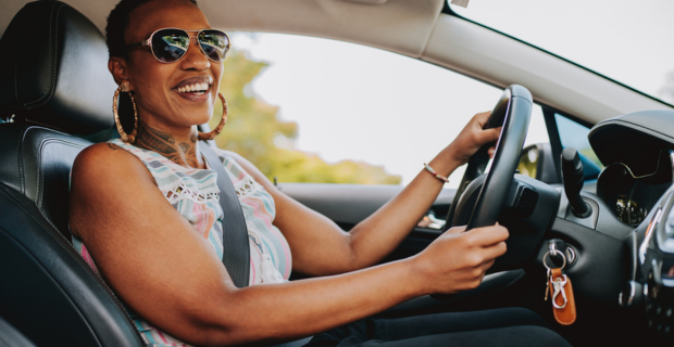 Une personne heureuse économisant sur l’entretien de sa voiture à l’intérieur de son véhicule, au volant et vêtue d’un t-shirt sans manches.