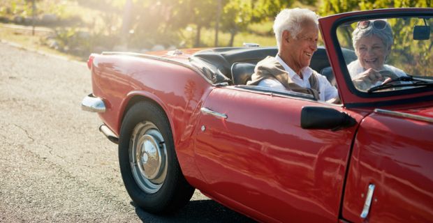 Image d’un couple âgé sur la route l’été dans leur voiture de collection. 