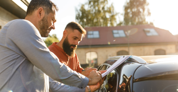 Deux personnes se tiennent à côté d'une voiture et discutent de documents, illustrant le processus d'achat d'une voiture au Canada et la considération des prix des voitures.
