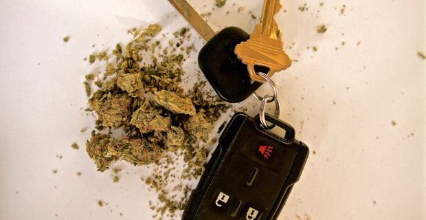Un ensemble de clés d’auto à côté d’une petite pile de cannabis séché sur un fond blanc.