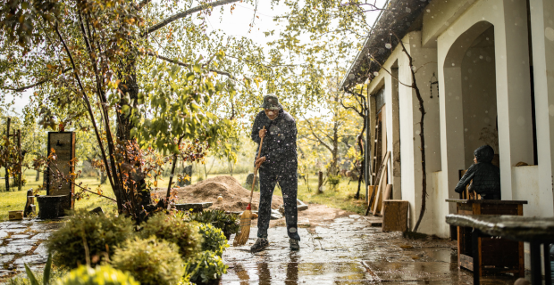 Un propriétaire dans sa cour arrière inondée, en train de balayer l'eau loin de sa maison par un jour de pluie.