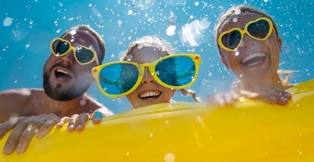 Scène d'été amusante avec trois personnes derrière un flotteur de piscine jaune, portant des lunettes de soleil et des lunettes de protection colorées, avec des éclaboussures d'eau et un ciel bleu vif.