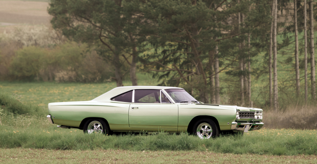 Une Plymouth Road Runner verte garée dans un champ herbeux près d’arbres.