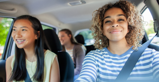 Une jeune au volant d’une voiture avec deux passagères, toutes attachées, voyageant ensemble par une journée ensoleillée.