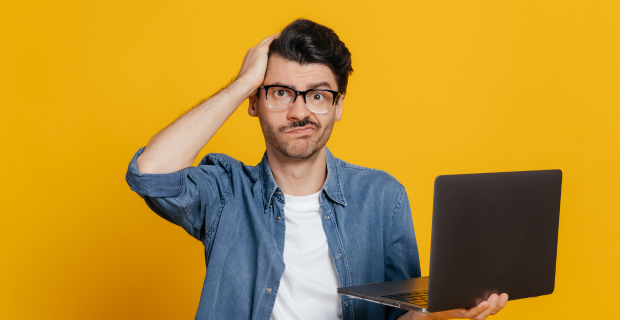 Un jeune adulte tient son portable d’une main et sa tête de l’autre. Il est debout et une expression confuse se lit sur son visage. L’arrière-plan est orange.