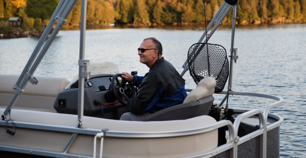 Une personne conduit un bateau avec, en arrière-plan, une rangée d’arbres aux couleurs d’automne.