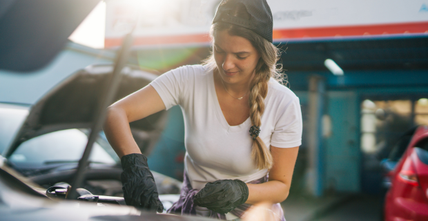 Une jeune femme regardant sous le capot d’un véhicule afin d’effectuer l’entretien printanier de sa voiture classique et de la préparer à prendre la route.