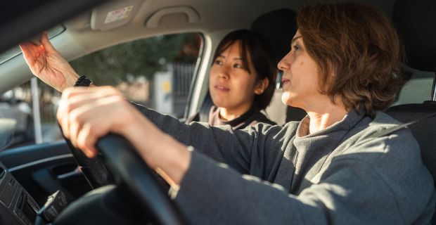 Deux femmes sont assises dans une voiture. La conductrice rajuste son rétroviseur.
