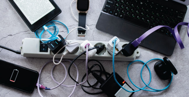 Multiprise surchargée avec plusieurs chargeurs et appareils électroniques, dont un smartphone, une tablette, une montre connectée et un ordinateur portable.