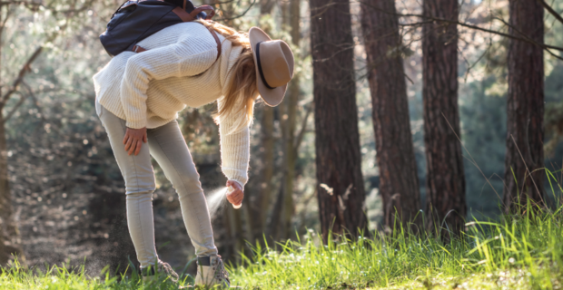Une femme se penche pour appliquer un spray anti tiques sur ses chevilles lors d’une promenade en forêt.