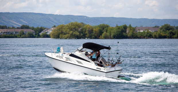 Bateau à moteur naviguant sur un lac canadien calme près d’une rive boisée.  