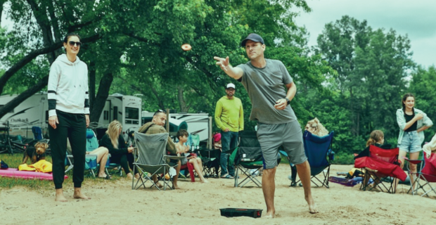 Homme jouant au jeu de washers sur un terrain de camping.