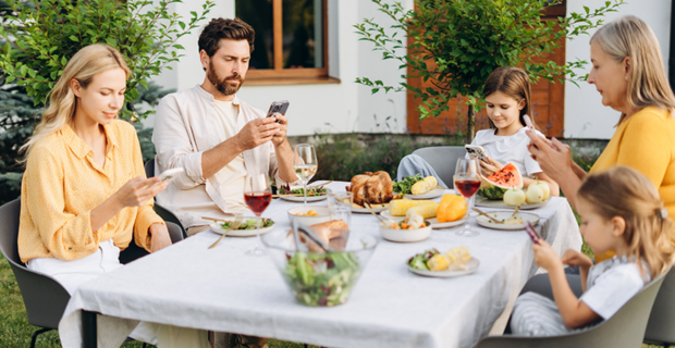 Une famille réunie autour de la table pour le repas, mais dont les membres sont absorbés par leurs écrans.