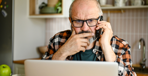 Personne utilisant un ordinateur portable et un téléphone pour vérifier une arnaque potentielle liée à l’IA chez elle.   