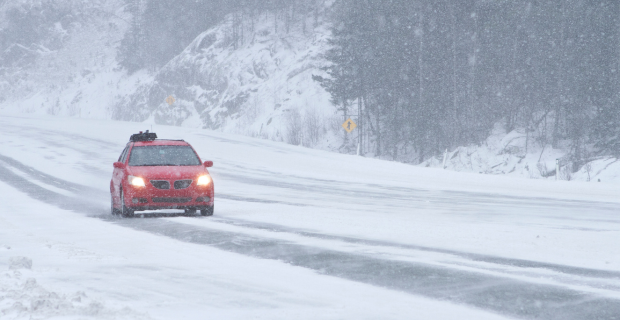 un véhicule rouge roulant sur une route enneigée, respectant les règles de sécurité routière en hiver.