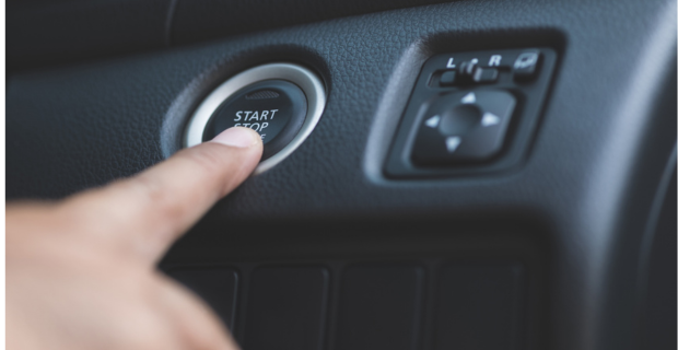 Image rapprochée d’un doigt au-dessus du bouton de démarrage sans clé du tableau de bord d’une automobile.